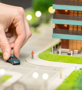 Diorama einer Hand, die ein Spielzeugauto durch Modellstadt fährt | © Shutterstock